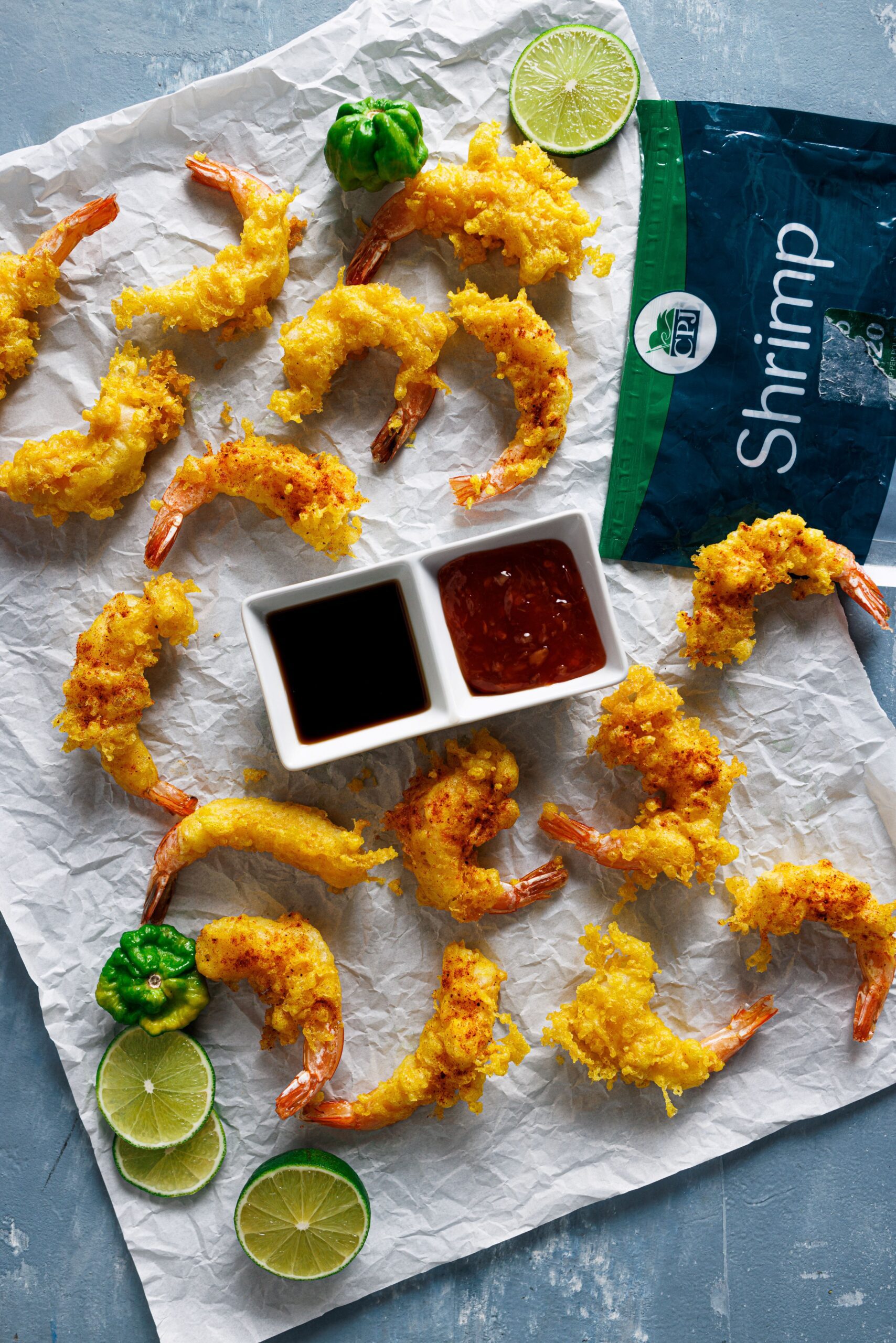 an overhead image of about one dozen fried shrimp tempura placed on a wax paper with dipping sauce in the middle