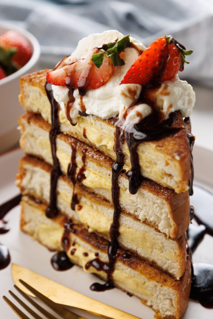 Easy Stuffed French Toast filled with cream cheese and passion fruit curd stack and covered in chocolate syrup strawberries and whipped cream