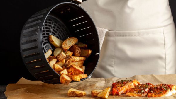 a chef pouring out roasted potatoes from an air fryer onto a table of air fried salmon steaks
