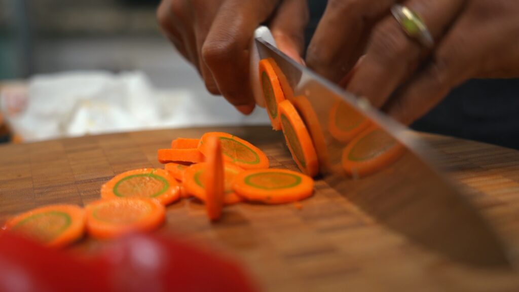 Carrot being sliced into thin rondels on a cutting board