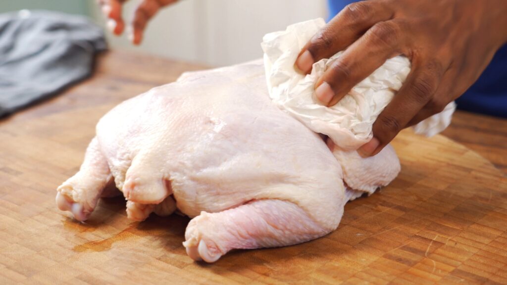 Chef Samantha patting uncooked chicken with paper towel to remove excess moisture