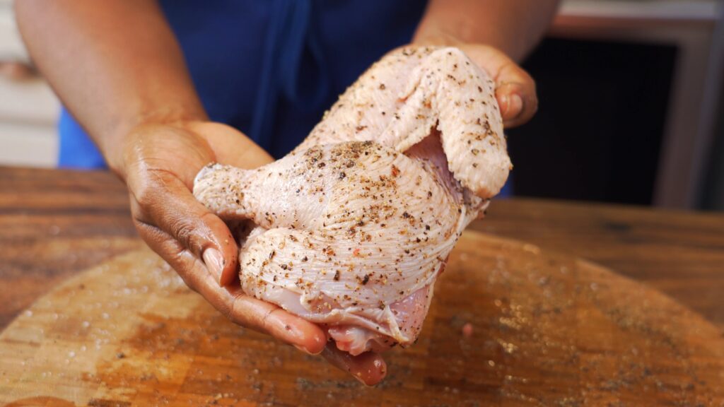 Close up shot of Chef Samantha holding a half chicken seasoned with fresh black pepper to prepare for roasting in air fryer